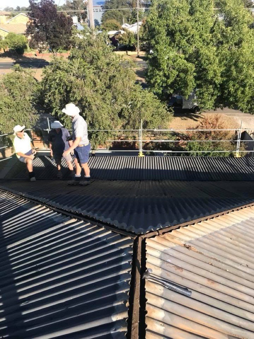 Two roofers in hard hats and hi-vis fixing dark steel sheets on a roof