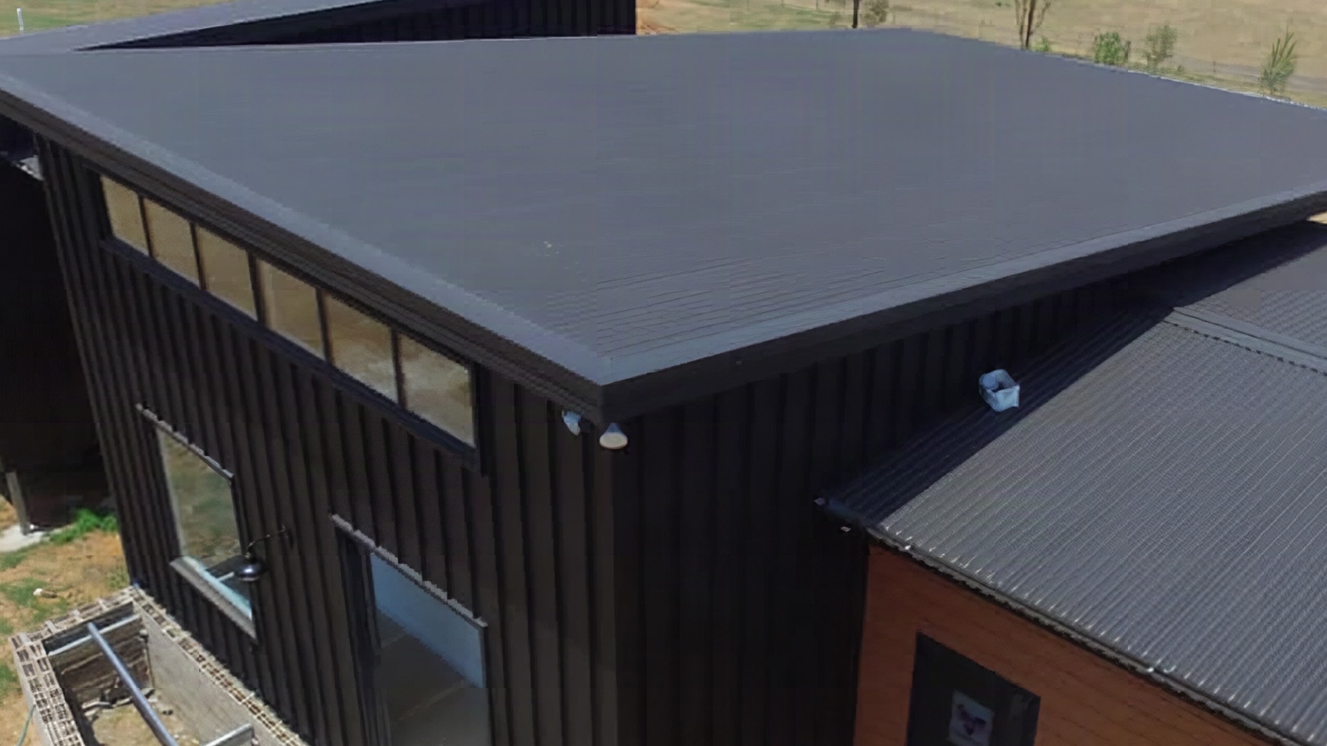 A dark steel roof on a building with open paddocks running behind it