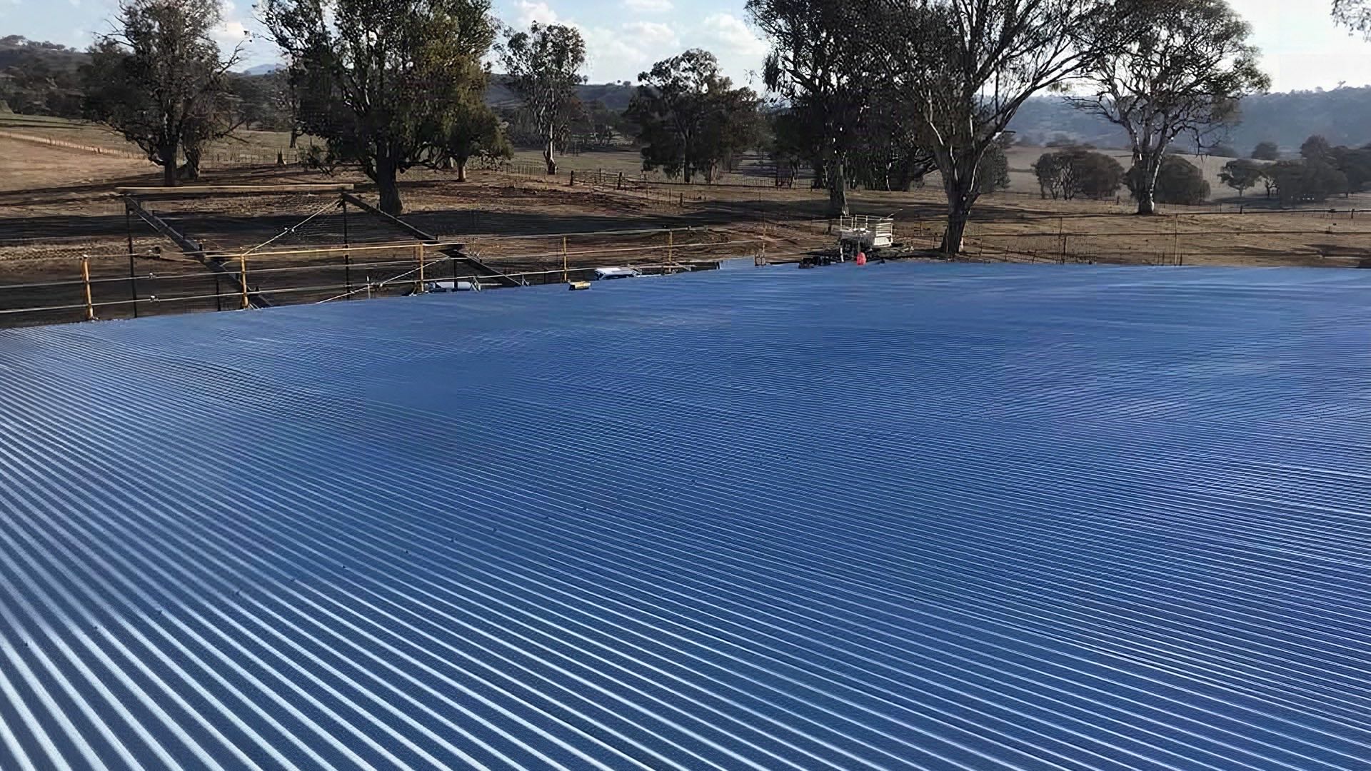 A wide blue Colorbond roof looking out over dry paddocks and gum trees