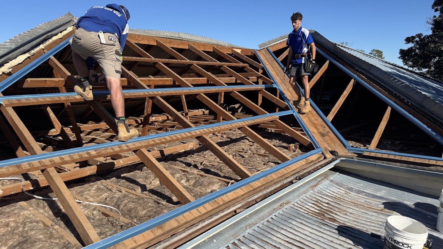 Two roofers working on the exposed timber rafters of a stripped roof