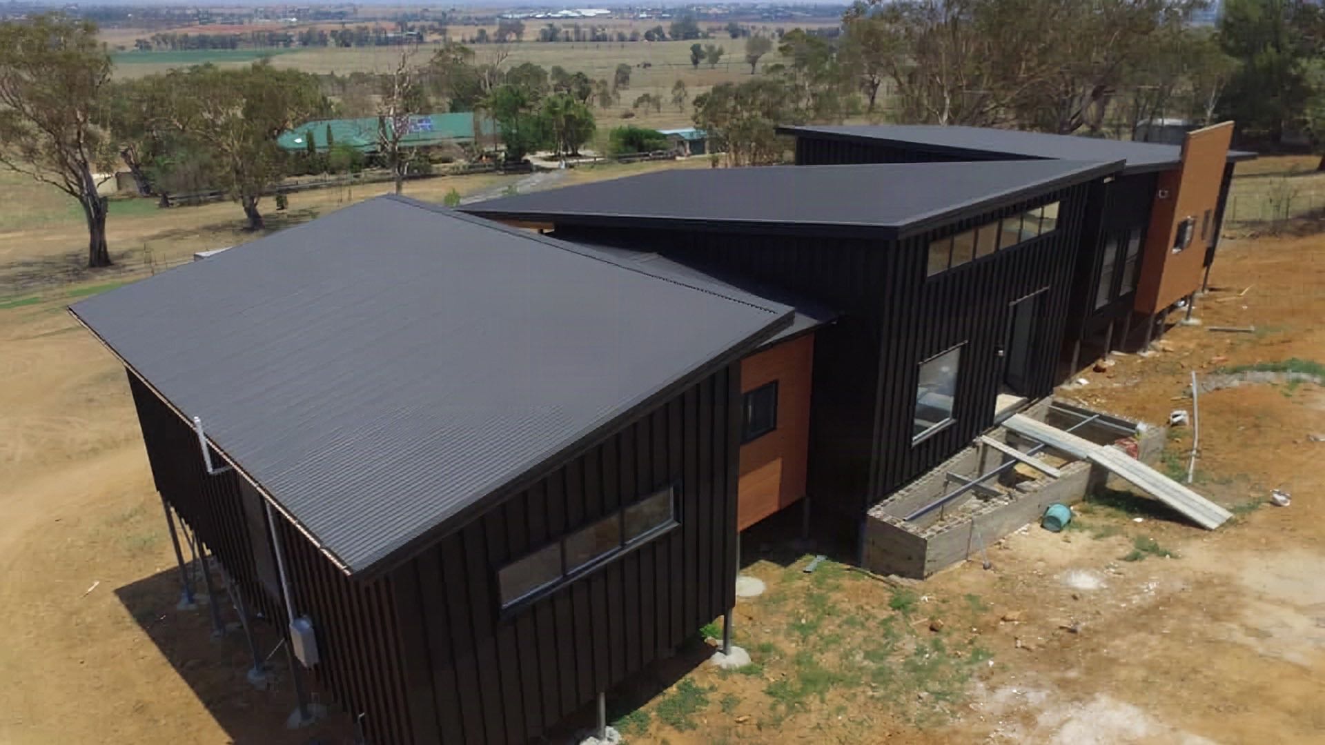 A dark Colorbond roof on a new home, with dry paddocks and gum trees behind it