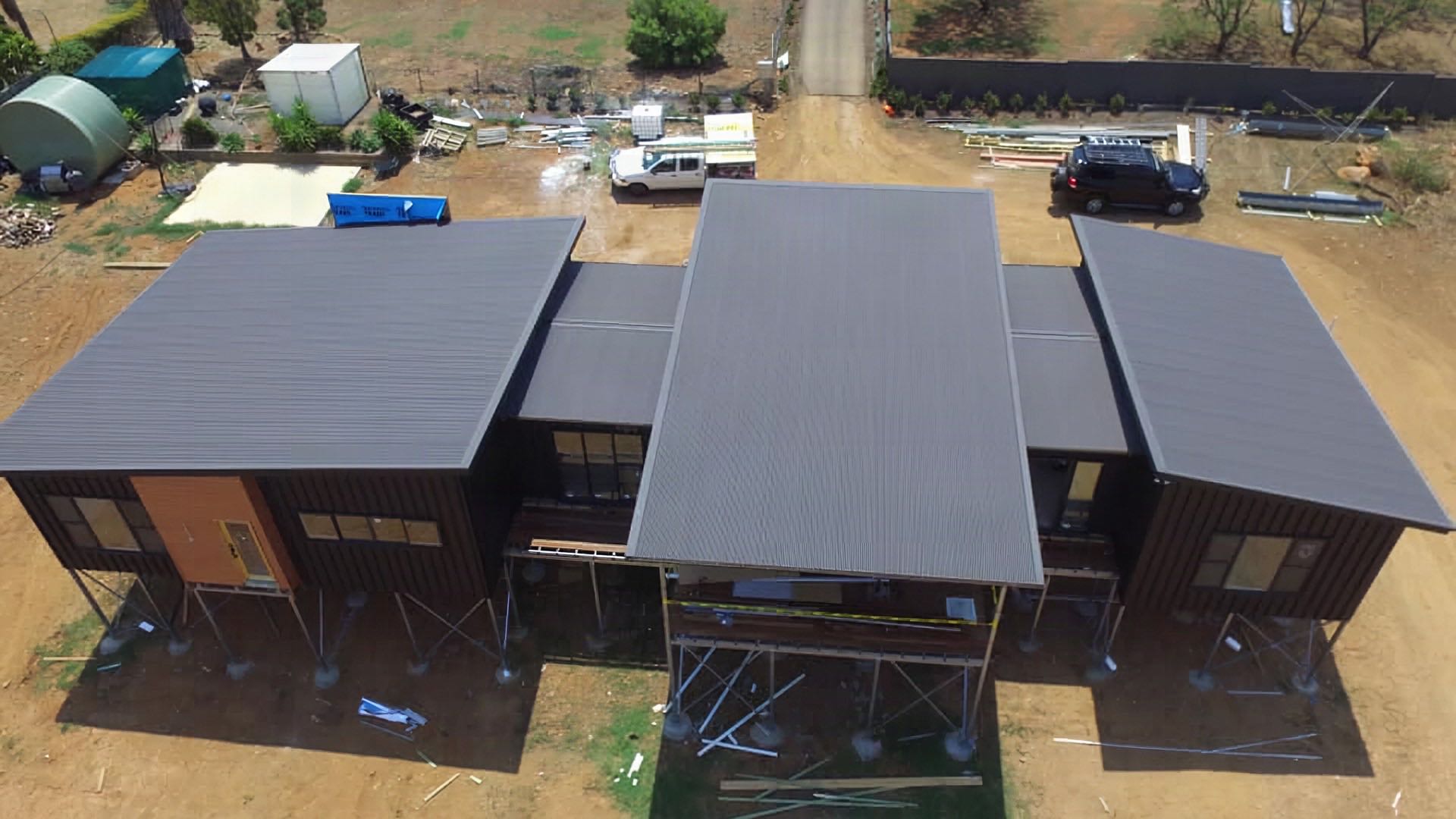 Dark steel roofs on a group of new buildings, seen from above on red-brown ground