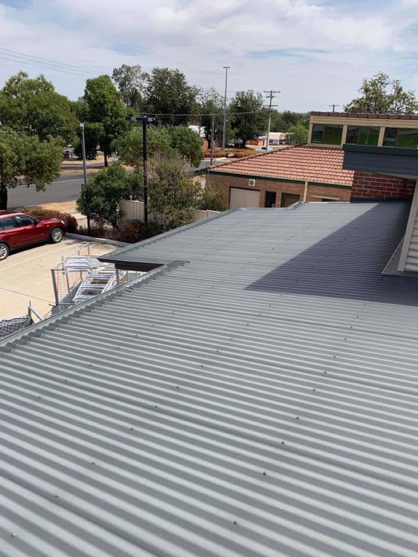 A new grey steel roof beside an older terracotta tile roof on the same street