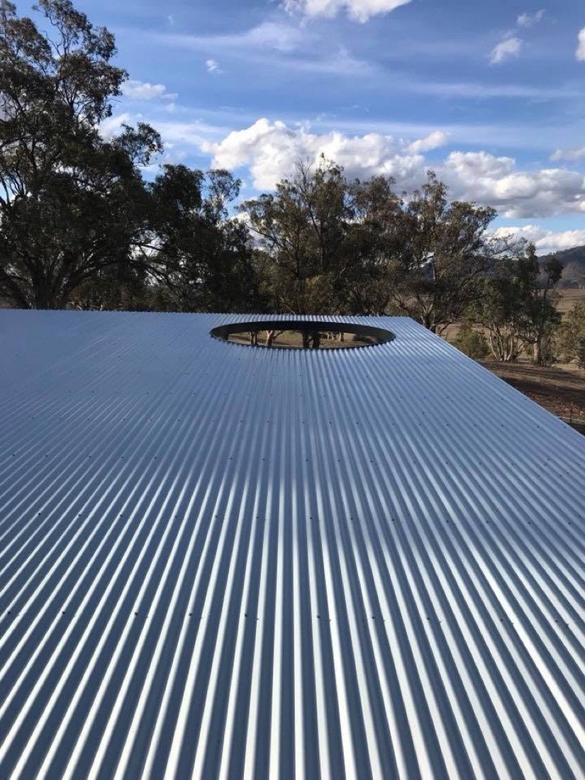 A round roof vent set into a dark steel roof under a blue sky