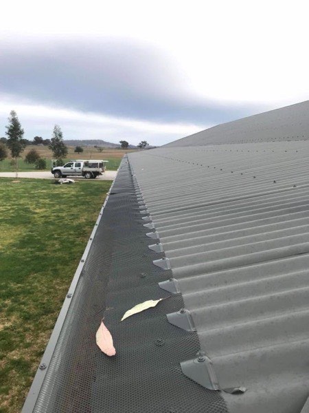 A grey steel roof with a work ute parked below and hills behind