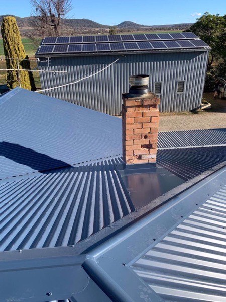 A blue steel roof meeting a brick chimney