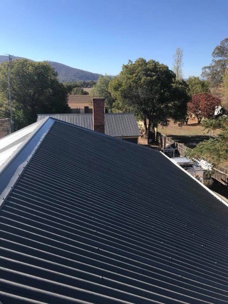 A dark steel roof with hills rising behind it