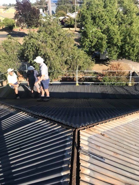 Two roofers in hard hats laying dark steel sheets on a roof