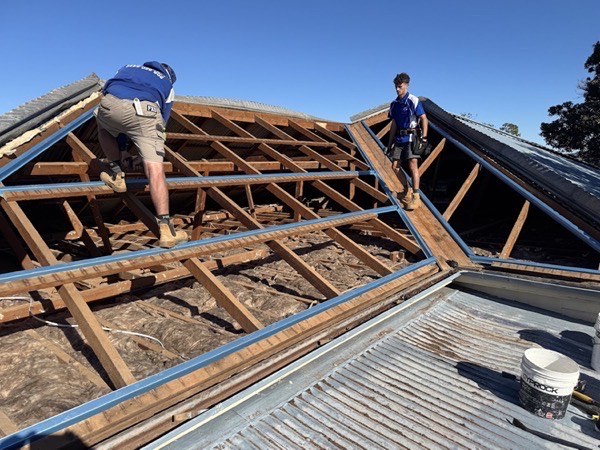 Two roofers working on the exposed timber rafters of a stripped roof